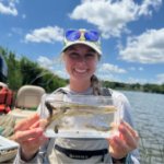 Emily Eberly holds a clear container containing several juvenile fishes to the camera. on March 27, 2026